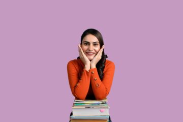 Joven estudiante sonriente y confiada apoyada sobre una pila de libros, representando la tranquilidad de saber qué examen oficial de inglés elegir