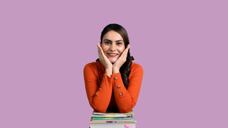Joven estudiante sonriente y confiada apoyada sobre una pila de libros, representando la tranquilidad de saber qué examen oficial de inglés elegir