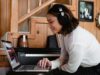 Estudiante sonriente con auriculares grandes puestos, mirando atentamente la pantalla de su ordenador portátil mientras practica la comprensión auditiva