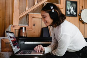 Estudiante sonriente con auriculares grandes puestos, mirando atentamente la pantalla de su ordenador portátil mientras practica la comprensión auditiva