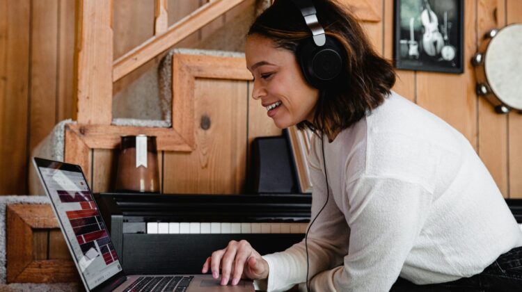 Estudiante sonriente con auriculares grandes puestos, mirando atentamente la pantalla de su ordenador portátil mientras practica la comprensión auditiva