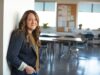 Mujer sonriente apoyada en la pared de un aula vacía, representando a una profesora que ha asegurado su plaza en las oposiciones gracias a los puntos de su certificado C1 de inglés