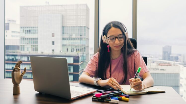 Alumna con auriculares tomando notas frente a un ordenador portátil, simulando la preparación de la prueba de comprensión auditiva y oral de inglés
