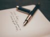 Pluma estilográfica clásica apoyada sobre un cuaderno con caligrafía elegante, representando la redacción de una carta o email formal en la prueba de Writing