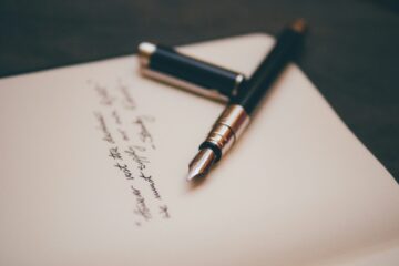 Pluma estilográfica clásica apoyada sobre un cuaderno con caligrafía elegante, representando la redacción de una carta o email formal en la prueba de Writing