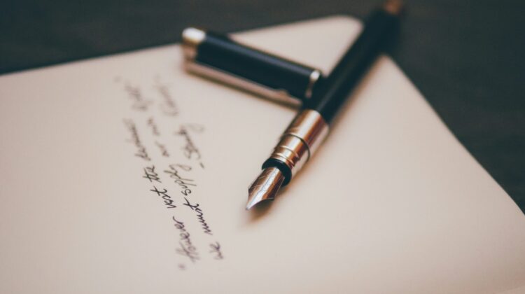 Pluma estilográfica clásica apoyada sobre un cuaderno con caligrafía elegante, representando la redacción de una carta o email formal en la prueba de Writing
