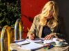 Mujer joven escribiendo relajadamente en una libreta mientras toma un café en una terraza soleada, representando la actitud natural necesaria para redactar un email informal en inglés
