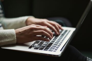 Primer plano de las manos de una persona tecleando en un ordenador portátil, representando la redacción de la prueba de Writing en un examen oficial de inglés