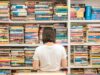 Mujer de espaldas mirando una enorme estantería llena de libros y diccionarios, representando la frustración de intentar memorizar interminables listas de Phrasal Verbs en inglés
