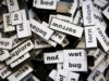 Primer plano de muchas piezas magnéticas con palabras en inglés desordenadas, representando la construcción de frases y la dificultad de traducir expresiones idiomáticas literalmente