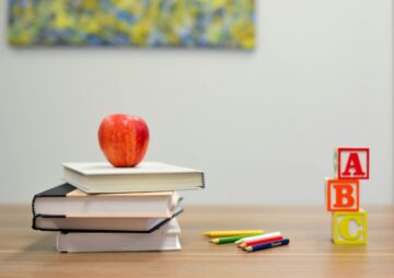 Manzana roja sobre una pila de libros y bloques del abecedario sobre un escritorio de madera, representando el baremo de méritos en las oposiciones de educación