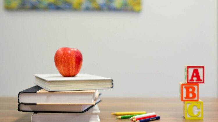 Manzana roja sobre una pila de libros y bloques del abecedario sobre un escritorio de madera, representando el baremo de méritos en las oposiciones de educación