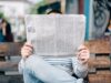 Persona leyendo un periódico impreso en papel, representando el formato periodístico y la lectura de artículos en inglés