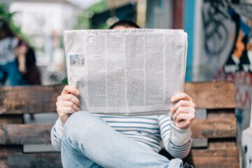 Persona leyendo un periódico impreso en papel, representando el formato periodístico y la lectura de artículos en inglés