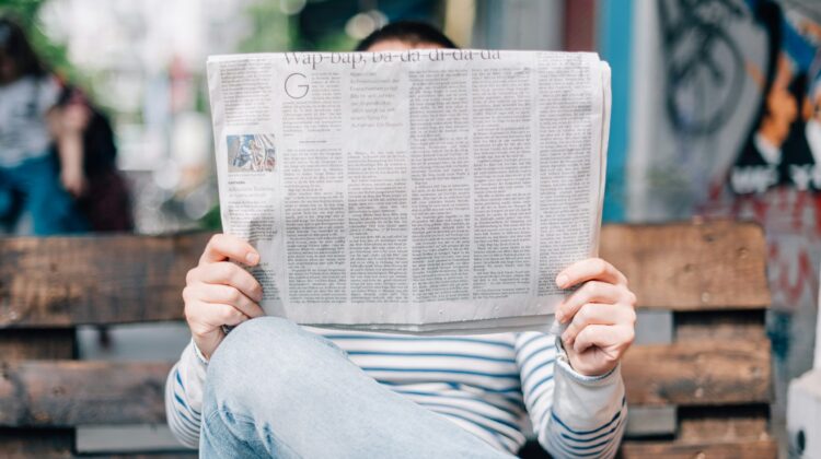 Persona leyendo un periódico impreso en papel, representando el formato periodístico y la lectura de artículos en inglés