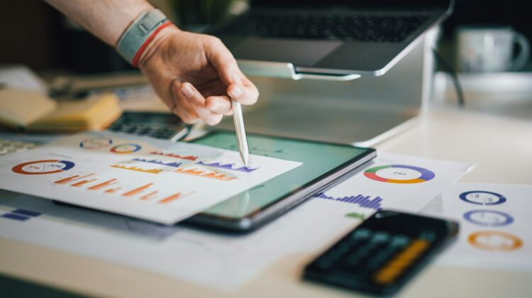Primer plano de una persona analizando gráficos y estadísticas con un lápiz digital sobre un escritorio, representando el enfoque analítico y corporativo de un informe formal en inglés
