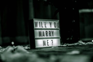 Cartel luminoso con el texto Will you marry me rodeado de pétalos, representando el juego de palabras del término Proposal en inglés