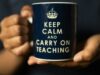 Persona sujetando con ambas manos una taza azul oscuro con el mensaje en inglés Keep Calm and Carry on Teaching