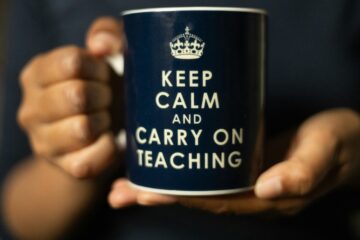 Persona sujetando con ambas manos una taza azul oscuro con el mensaje en inglés Keep Calm and Carry on Teaching