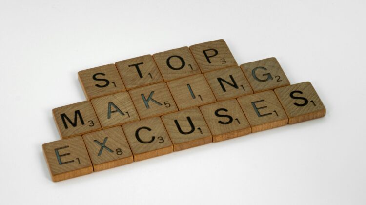 Fichas de Scrabble de madera sobre fondo blanco que forman la frase en inglés "Stop making excuses" (Deja de poner excusas).