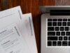 Varias hojas impresas con plantillas de trabajo, entre ellas «User Persona» y «Brand Colours», sobre una mesa de madera junto al teclado de un portátil
