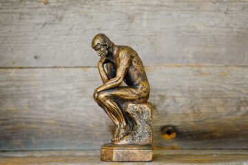 Pequeña estatua de bronce de El Pensador apoyada sobre una superficie de madera rústica