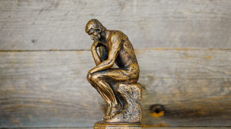 Pequeña estatua de bronce de El Pensador apoyada sobre una superficie de madera rústica